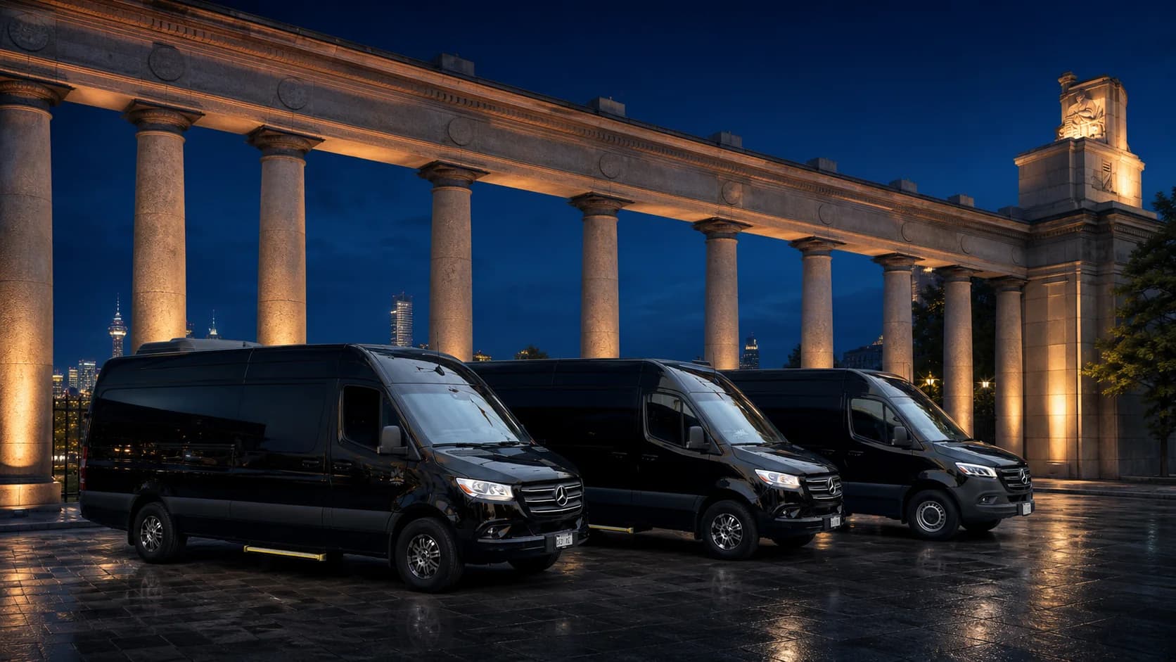 Three black Mercedes-Benz Sprinter vehicles beneath illuminated architectural columns